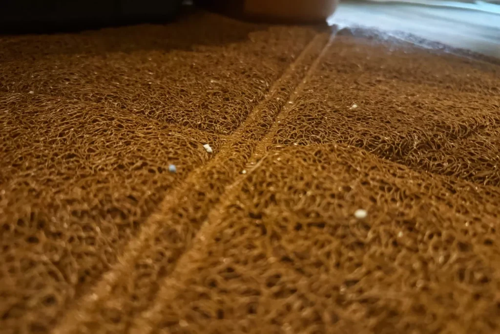 The 7 Best Cat Litter Mats for a Cleaner Home (Tested by Real Cats) 15 Extreme close-up of the brown, tangled, spaghetti-like texture of a mat, with a diagonal embossed line from its pattern visible and small white debris particles scattered on the surface.